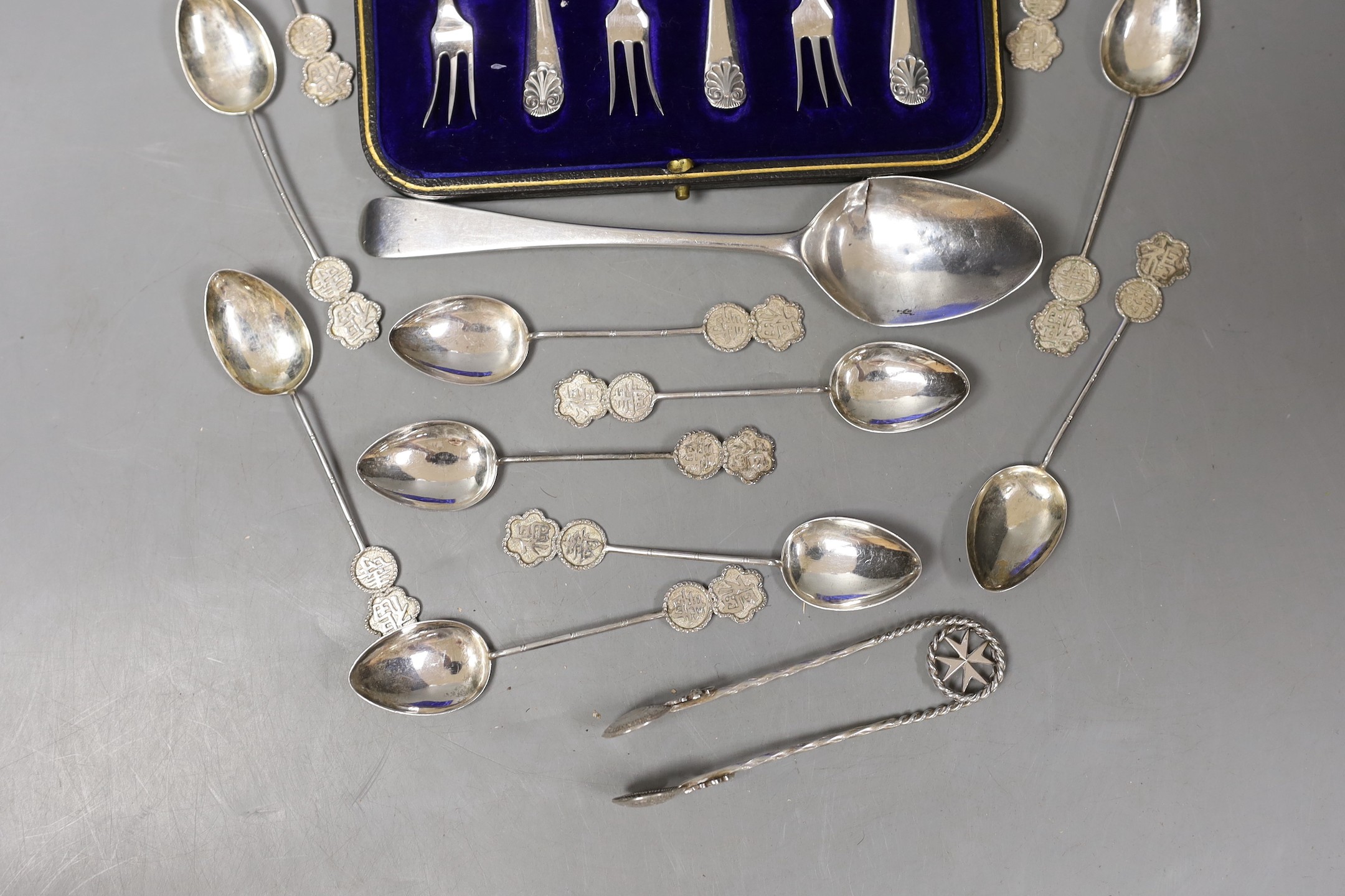 A cased set of six George V silver cake forks, a set of eleven Chinese white metal coffee spoons, a Georgian silver dessert spoon and a pair of white metal sugar tongs.